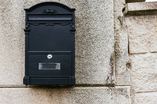A retro looking black mailbox, or letterbox, taped to the white exterior wall