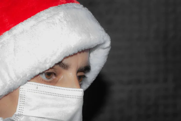 Side view of person in surgical mask wearing red Santa Claus hat isolated on black background. Protection against viruses, prevention of infections. Empty copy space for text.