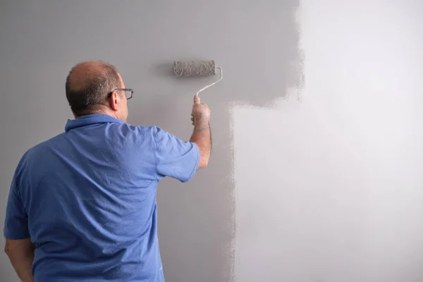 Real senior house painter painting a grey wall with a paint roller. Real dirty worker. House painter profession concept.