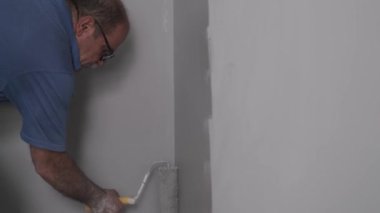 Gerçek bir son sınıf boyacısı gri bir duvarı boya rulosuyla boyuyor. Çok pis bir işçiydi. Boyacı mesleği kavramı.