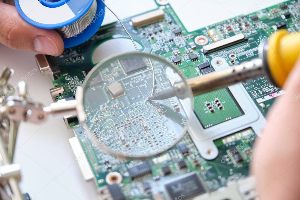 Repairing a printed circuit board with a soldering iron through a magnifying glass. Technology concept.