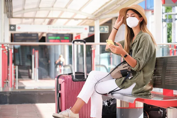 Mujer Joven Con Mascarilla Sombrero Usando Smartphone Mientras Espera Tren — Foto de Stock