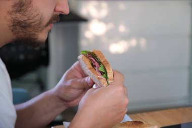 Pastırmalı sandviç yiyen bir delikanlıyı yakından çek. Fast food konsepti.