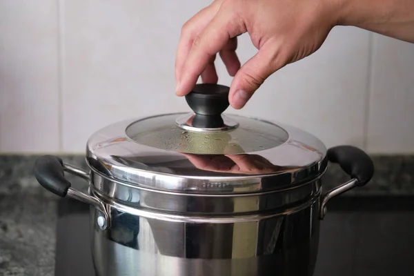 Unrecognizable hand lifting the lid of the steamer. Cooking pot.