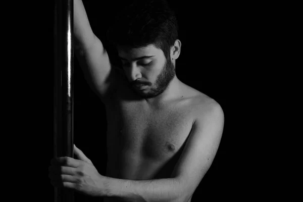 Dramatic dark portrait of a young man with a pole dance bar. Dark background studio shot. Black and white image.