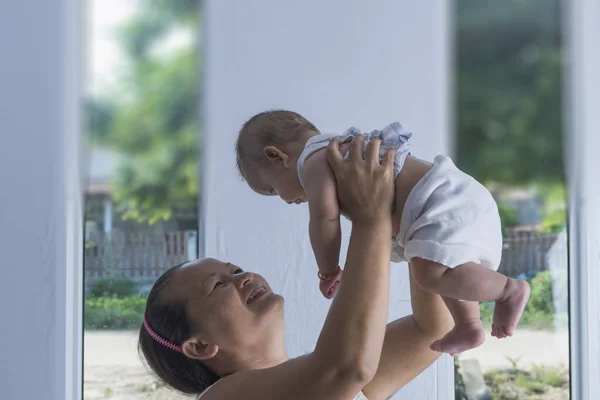 Asyalı bir annenin portresi. Yeni doğmuş bir bebekle oynayıp kaldırıyor, annesiyle konuşuyor. Sağlık hizmetleri aile sevgisi. Asyalı kız yaşam tarzı. Asya Anneler Günü konsepti.