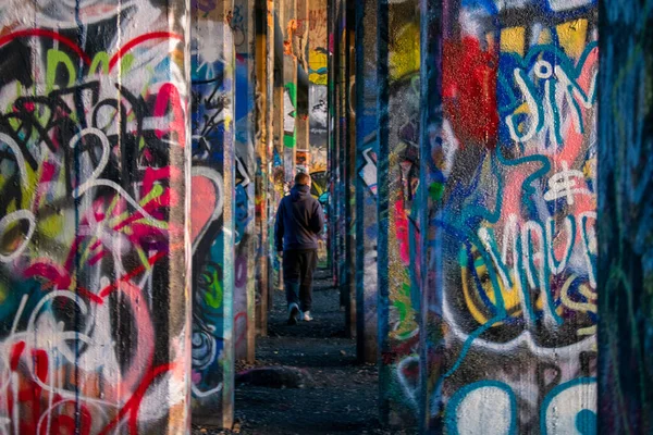 A Young Man Inbetween a Row of Graffiti Covered Walls at Graffiti Pier