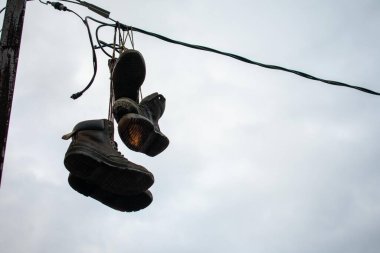 Bulutlu bir gökyüzünde ince bir kablodan sarkan botlar