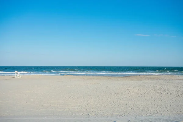 Wildwood New Jersey 'de açık mavi gökyüzünde cankurtaran sandalyesi olan büyük, boş bir sahil ve okyanus.