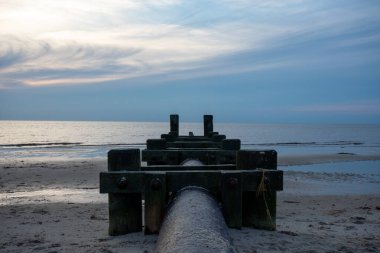 Her iki tarafında tahta direkler olan büyük bir boru okyanusa doğru uzanıyor.