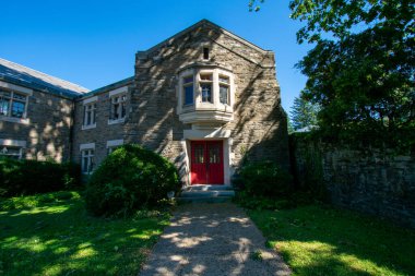 Açık mavi gökyüzündeki kırmızı kapıya giden yolu olan bir kaldırım taşı kilisesi.