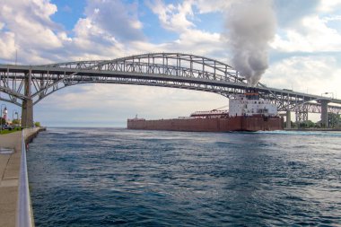 Port Huron, Michigan, USA - September 4, 2018: Great Lakes freighter the James Barker passes under the International Blue Water Bridge between Port Huron and Sarnia, Ontario, Canada. The border crossing is one of the busiest in the United States.  clipart