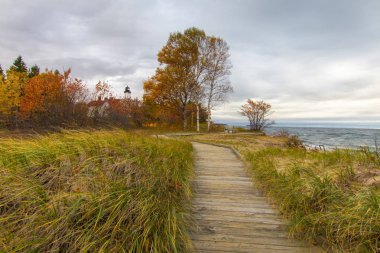 Boardwalk On Beach. Boardwalk trail through dune grass with the Point Iroquois lighthouse and the water of Lake Superior at the horizon in the Upper Peninsula of Michigan. clipart
