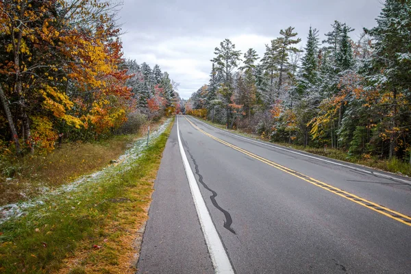 Remote Rural Road. Long road through the remote wilderness of northern Michigan surrounded by fall foliage with fresh fallen snow.