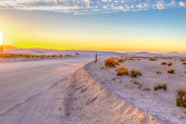 Uzak Çöl Yolunda Gün Batımı. New Mexico'daki White Sands Ulusal Anıtı'ndaki Beyaz Kumlar'ın çorak çölüboyunca uzun dolambaçlı uzak bir yol boyunca gün batımı.