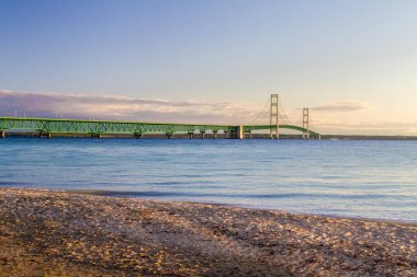 Mackinaw Köprüsü Panorama. Ön planda Michigan Gölü 'nün sakin mavi suyuyla Mackinac Köprüsü' nde sabah ışığı. Ünlü asma köprü Michigan eyaletinin Yukarı ve Aşağı Yarımadasını birbirine bağlıyor..