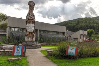 Cherokee, Kuzey Carolina, ABD - 12 Ağustos 2020: Cherokee Kızılderili Müzesi 'nin dışındaki Büyük Totem Kutbu yüz maskesi ve COVID -19' un yayılmasını yavaşlatmak için maske takıyor..
