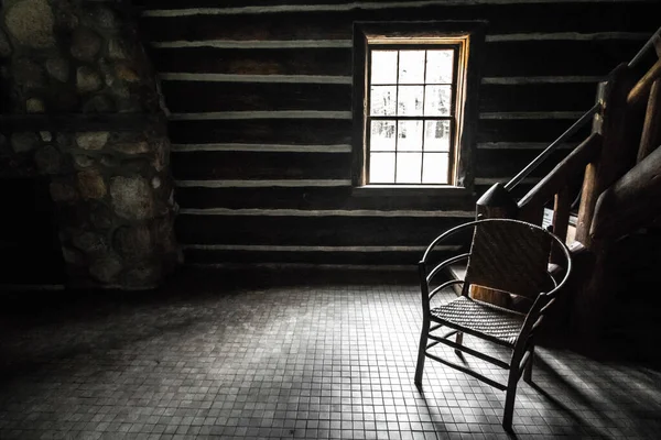 Empty Room With Single Chair. Sunlight streams through the window of a cabin with an empty wooden chair in the corner. This is the interior of a state owned historical building and not a private property or residence.