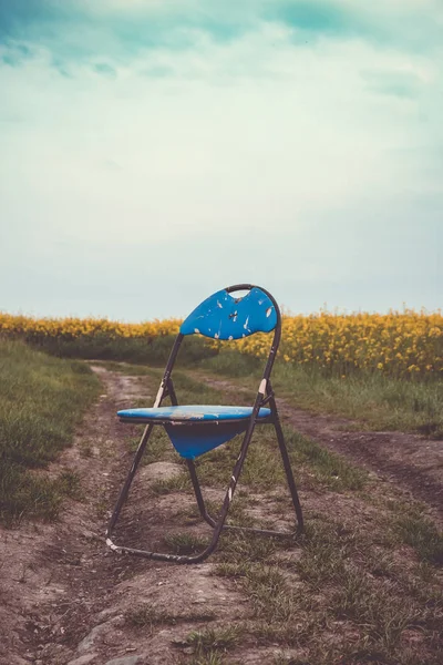 Vieille chaise pliante bleue à côté d'un champ de viol — Photo