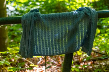 Hassas bir kumaş parçası, parlak yeşil yaprakların arasından süzülen hafif güneş ışığıyla aydınlatılan yosun kaplı bir korkuluğun üzerinde duruyor. Doğa bu huzur ortamını sarmış..