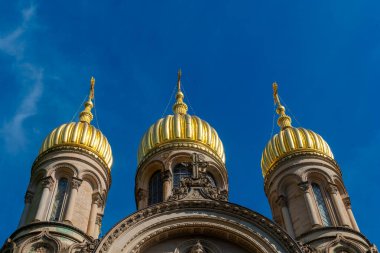 Üç görkemli altın kubbe güneş ışığını yansıtan canlı mavi gökyüzüne karşı dimdik ayakta duruyor. Mimarinin karmaşık ayrıntıları bu tarihi mekanın ihtişamını ve işçiliğini vurguluyor..