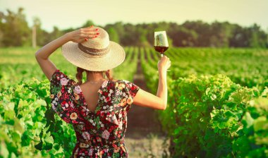 Asyalı bir kadın tatil sırasında üzüm bağında kırmızı şarap içiyor.