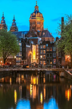 Aziz Niklas Kilisesi eski kasaba kanalı üzerinde geceleyin aydınlatılmış Amsterdam, Hollanda