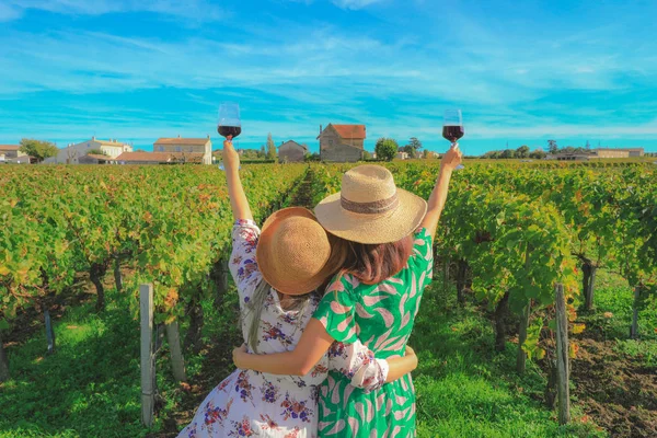 Tatilde üzüm bağında kırmızı şarap içen kadınların arkasında parti konsepti var.