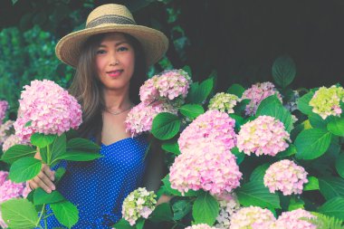 Bahçesinde pembe ortanca çiçekleri olan Asyalı bir kadın.