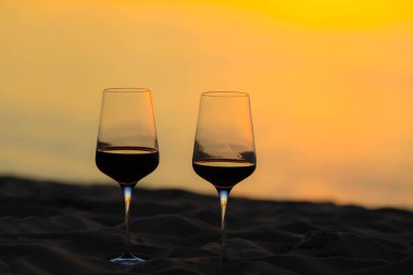 Gün batımında sahilde kırmızı şarap kadehleri, kutlama konsepti.