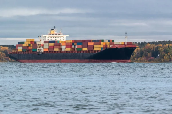 Container cargo ship cruising near a house along the river