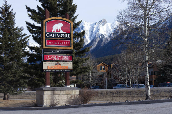 Кэнмор, Канада - апрель 2020 года: Вид на вход Canmore Inn and Suites Hotel с соснами и горами на заднем плане