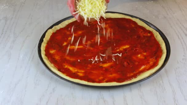 Frau bestreut Pizza mit geschreddertem Käse. — Stockvideo