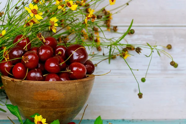 Red ripe cherries with stem in bowl with flowers.
