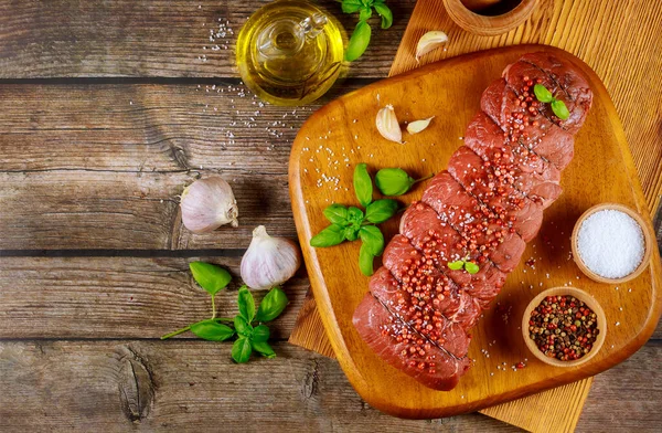 Uncooked beef steaks with spice and oil on wooden board.