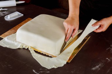 Kare pastaya beyaz fondantı kesen pastacı. Düğün pastası yapma tekniği..