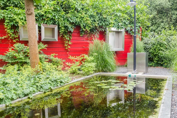 Дизайн сада с прудом и красной стеной — стоковое фото
