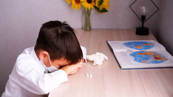 El niño no va a la escuela está enfermo en casa con una máscara y toma pastillas. Educación remota. — Foto de Stock