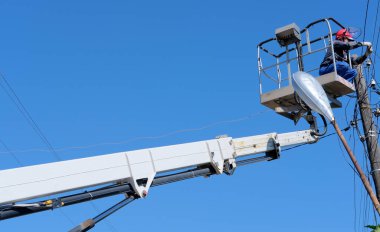 Lektrisyen adam vinç kullanarak elektrik hatları ve direkleri servis ediyor.