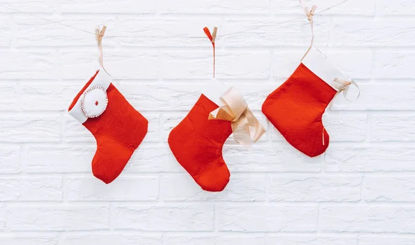Red and white christmas stockings hanging from a clothesline against a white brick wall background holiday