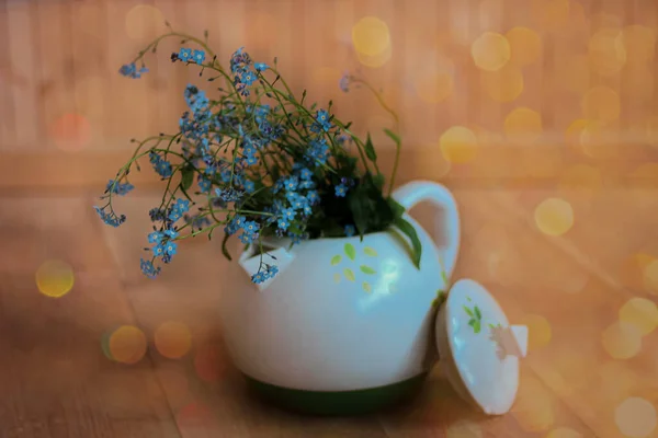 Ahşap bir zeminde, beyaz bir çaydanlıkta mavi çiçekler