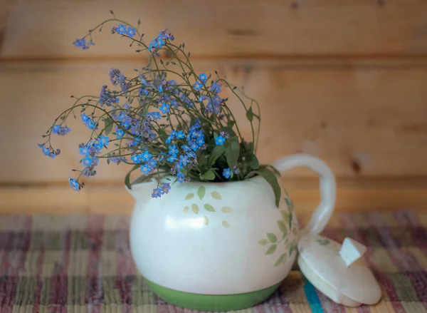 Beyaz bir çaydanlıktaki mavi çiçekler dokunmuş bir halıya, seçici bir odak