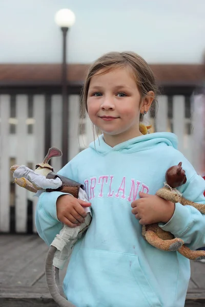 Oyuncak tavşan ve oyuncak ayı taşıyan yeşil ceketli bir kız ayakta duruyor.