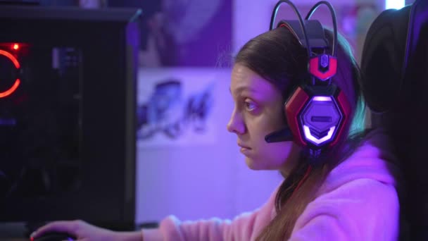 A young girl puts on gaming headphones and looks perplexed at the monitor. — Stock Video