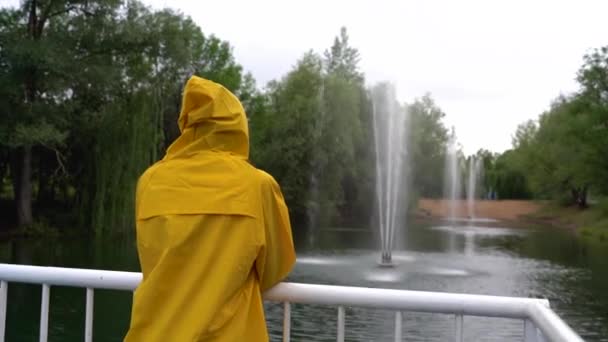 Une jeune fille en imperméable jaune regarde les fontaines. — Video
