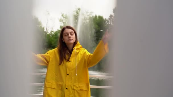 Krásná dívka ve žlutém plášti se opírá o bílý plot. — Stock video