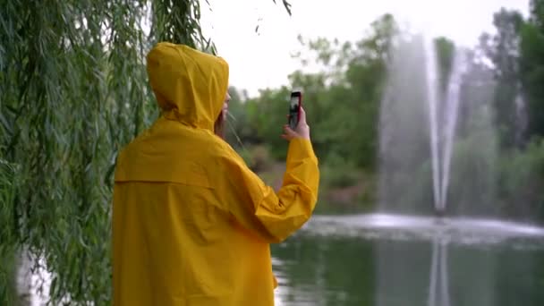 Mädchen in gelbem Regenmantel geht und macht Fotos mit dem Handy — Stockvideo