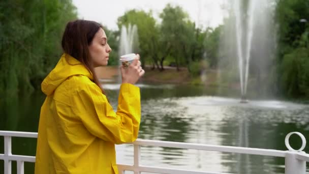 Dívka drží šálek kávy v rukou a užívá si. Rybník s fontánami — Stock video