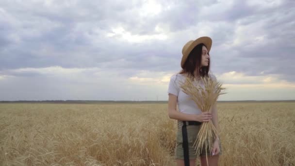 Chica joven en un sombrero de paja se encuentra en un campo de trigo. — Vídeos de Stock