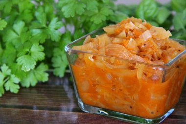 Şeffaf bir fincanda, ahşap bir masada taze yeşilliklerin arka planında haşlanmış lahana.